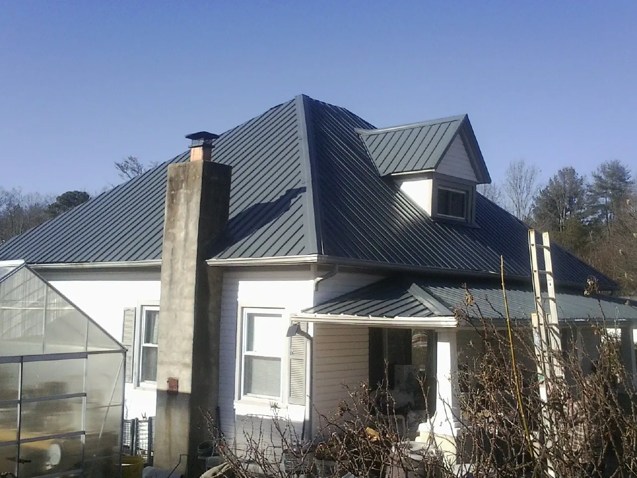 Dark blue standing seam metal roof on a white farmhouse with dormer — Slate & Tile Roof Repair by Roofing Brothers in Powers