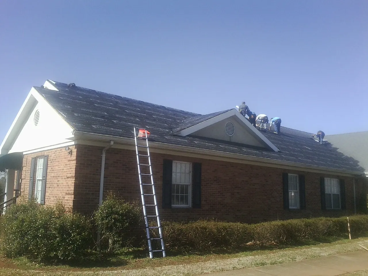 Crew tearing shingles off a brick ranch roof with a ladder set — Emergency Roof Repair work by our crew in Powers