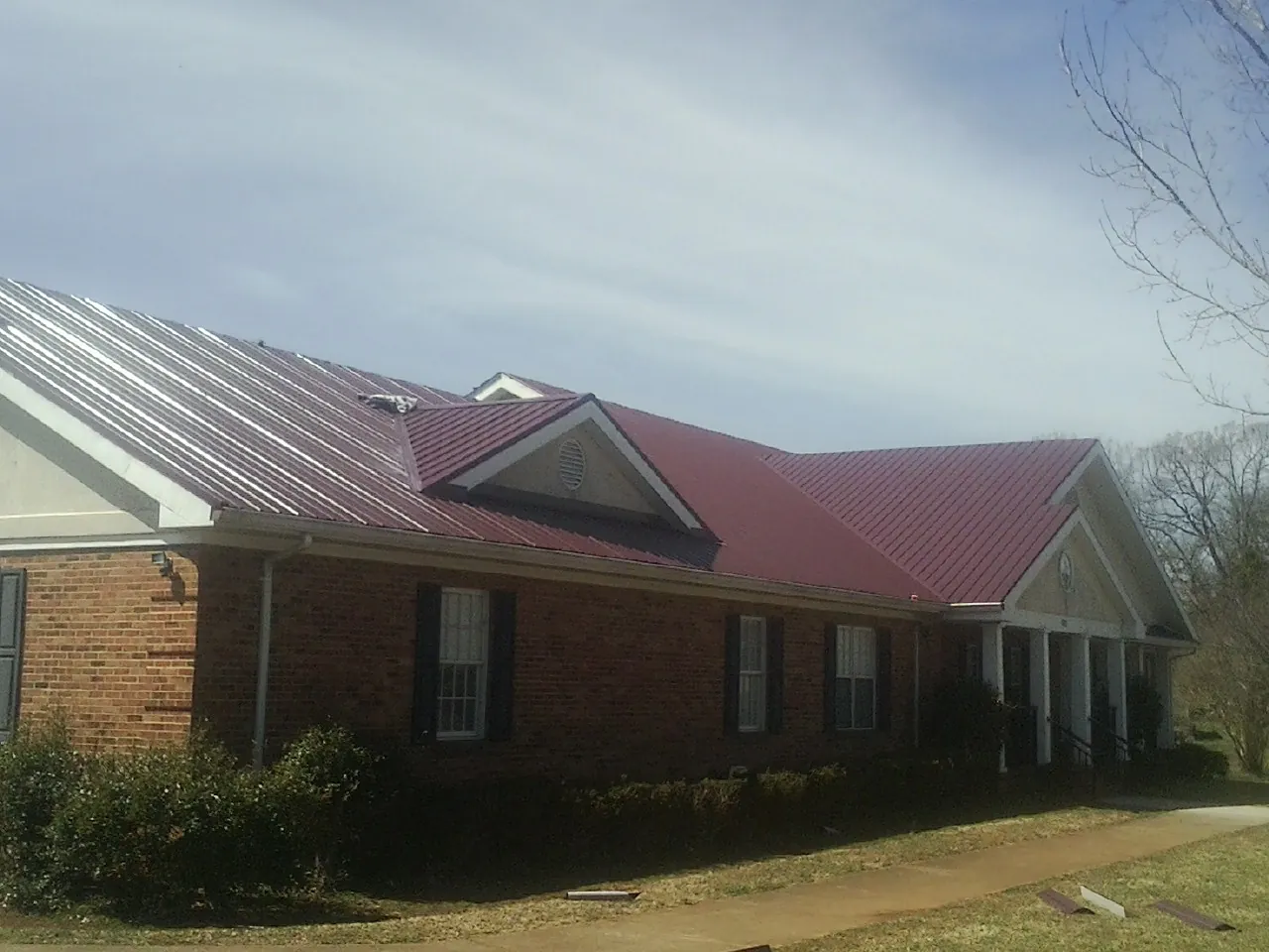 Red metal roof with gabled entries on a long brick building, from a Hail Damage Roof Repair job in Powers