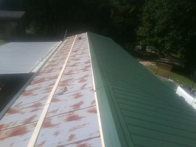 Old rusted panels beside newly installed green metal roofing — Wind Damage Roof Repair by Roofing Brothers in Powers