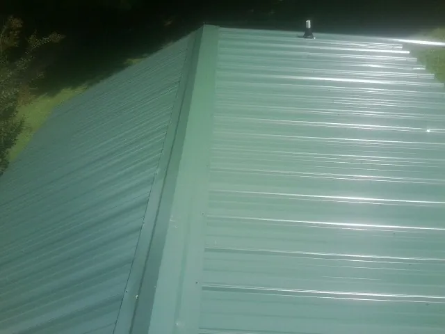 New green metal panels meeting at the ridge of a roof — Flat Roof Repair work by our crew in Powers