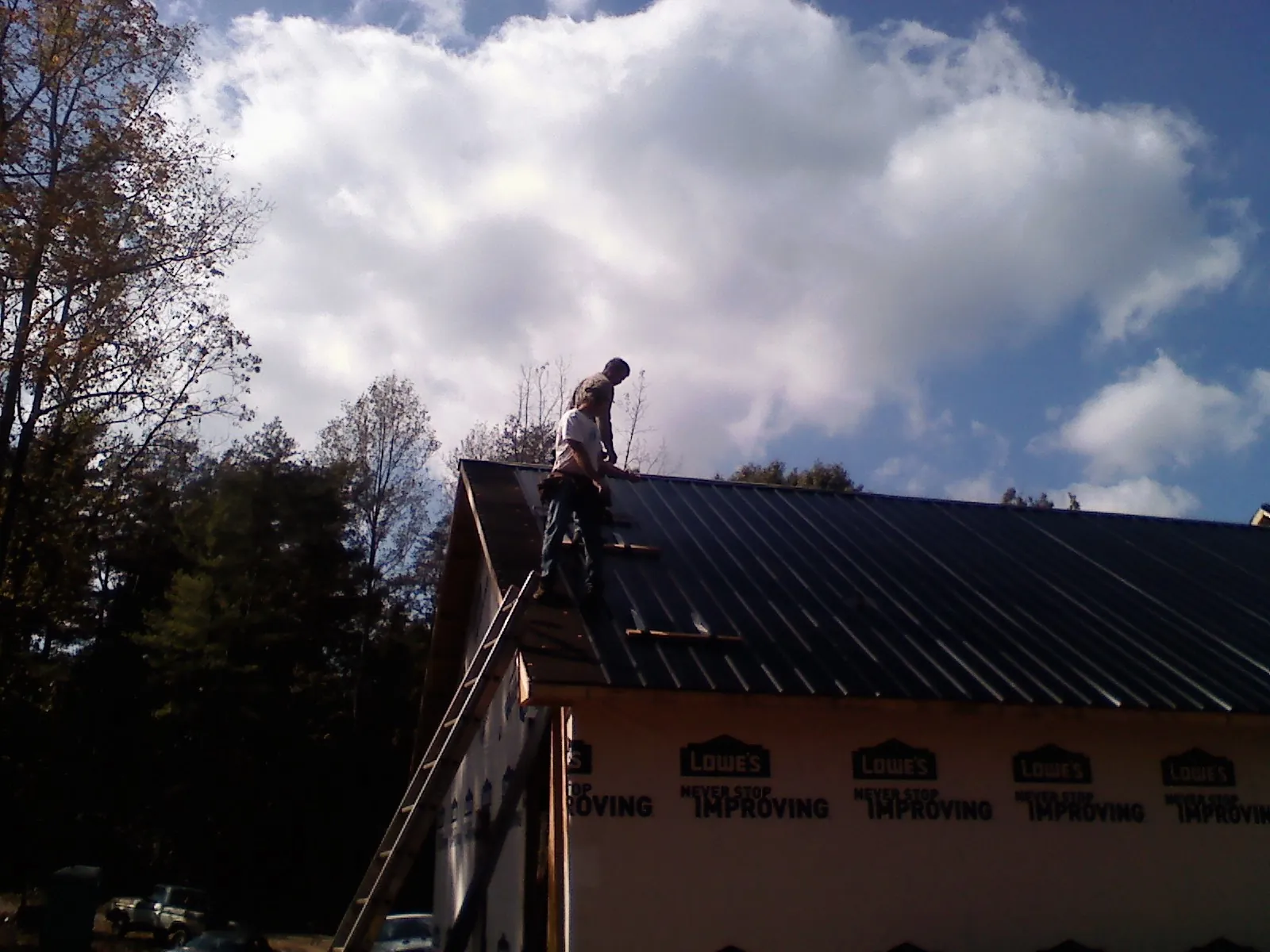 Roofer fastening dark metal panels high against a cloudy sky, from a Roof Inspection job in Powers